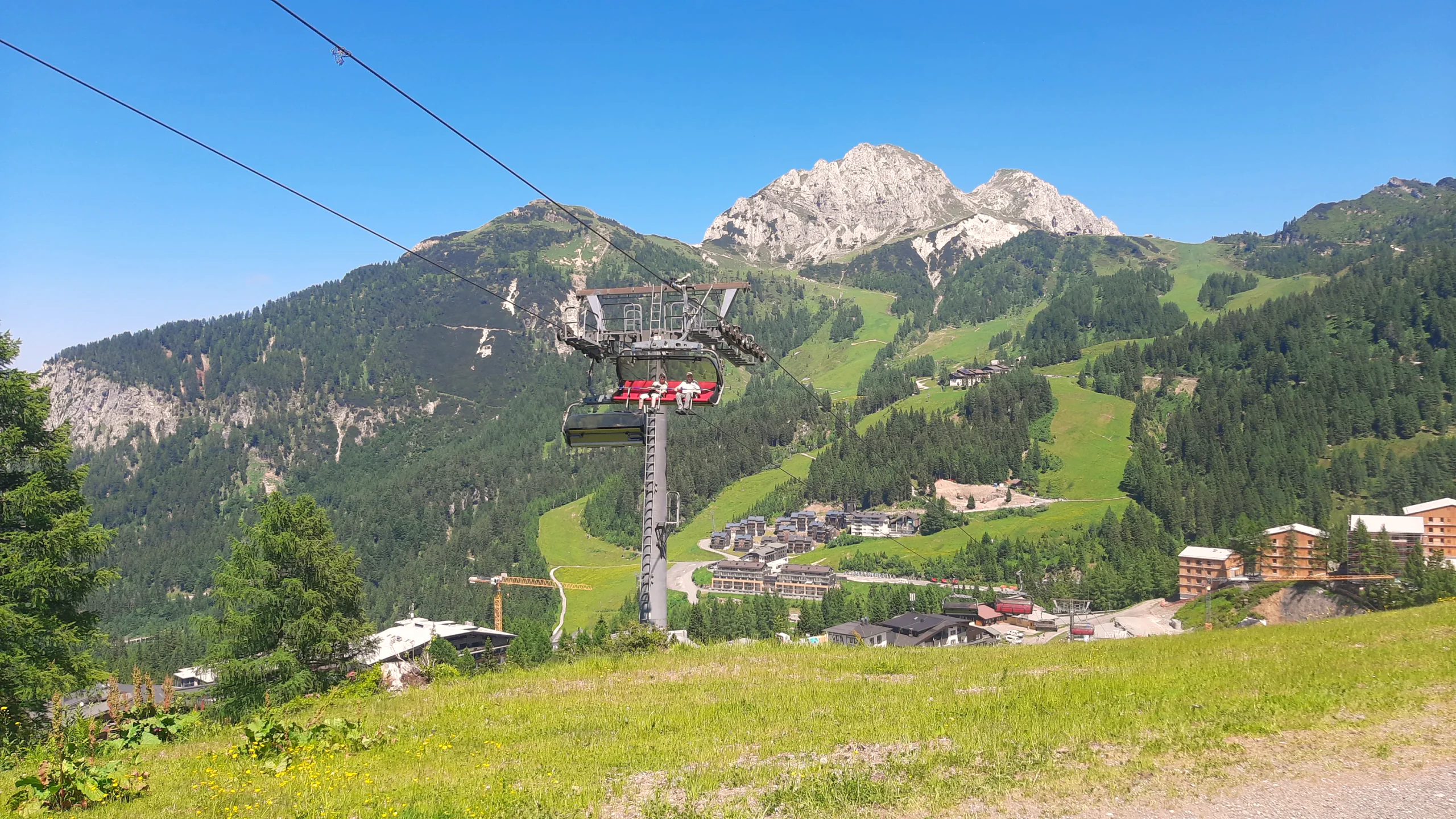 Sessellift über grünen Almhängen am Nassfeld, dahinter felsige Gipfel unter blauem Himmel