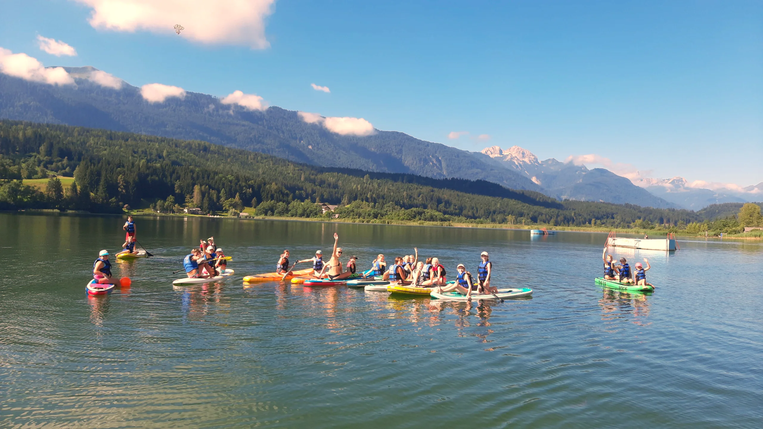 Eine Gruppe auf Stand-up-Paddle-Boards auf dem Pressegger See vor Bergkulisse