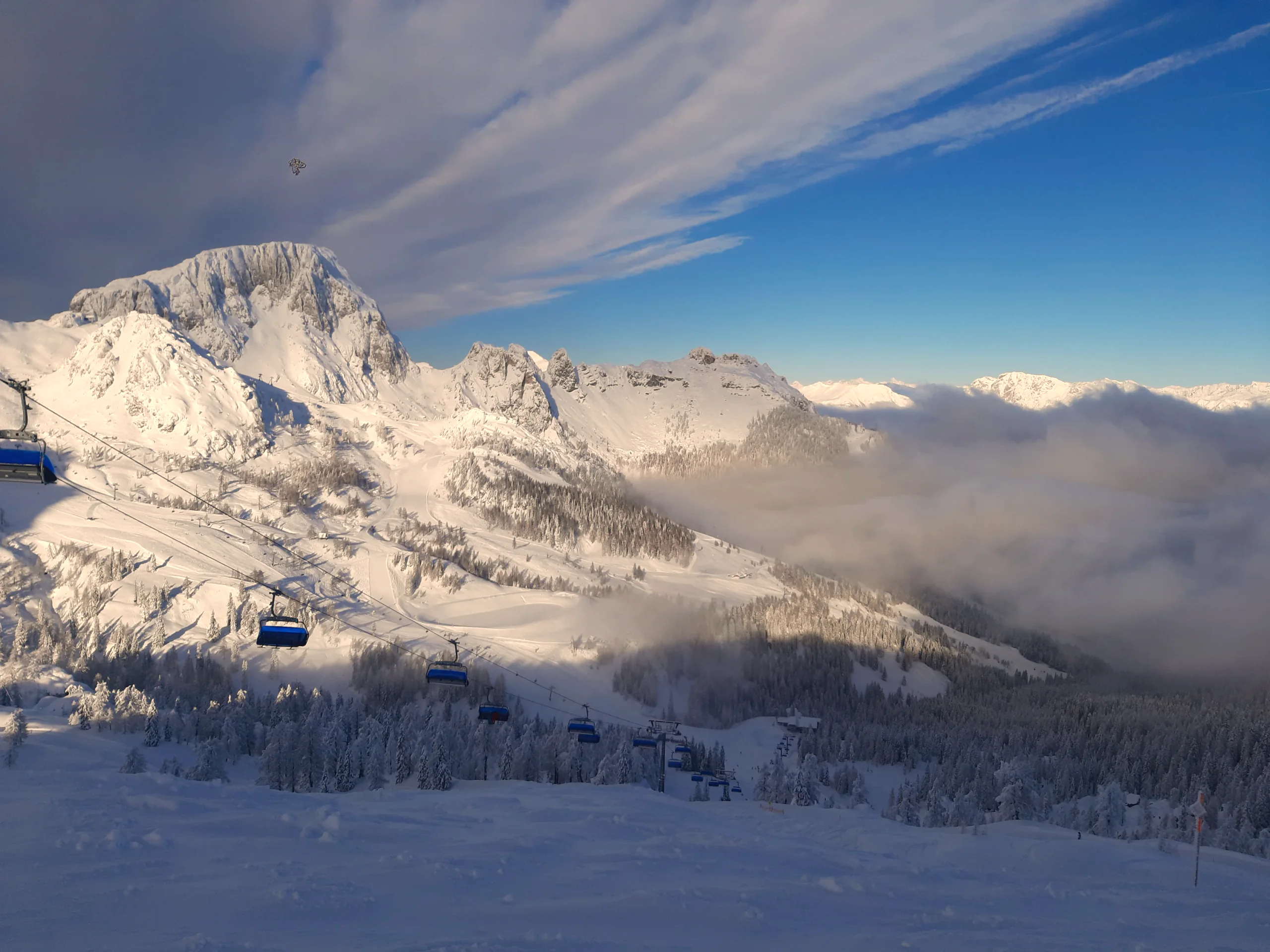 Sessellift am Nassfeld im Winter: blaue Sessel über verschneiten Hängen, die Gipfel dahinter in Wolken