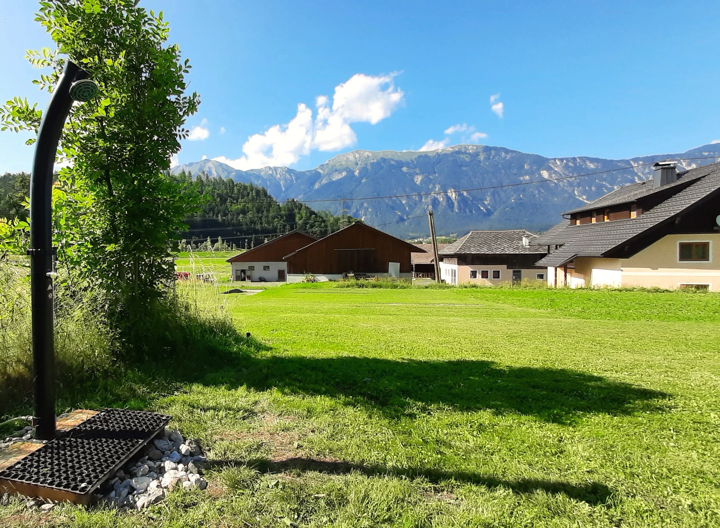 Schwarze Außendusche am Rand der Stellplatzwiese, dahinter Höfe und die Gailtaler Berge