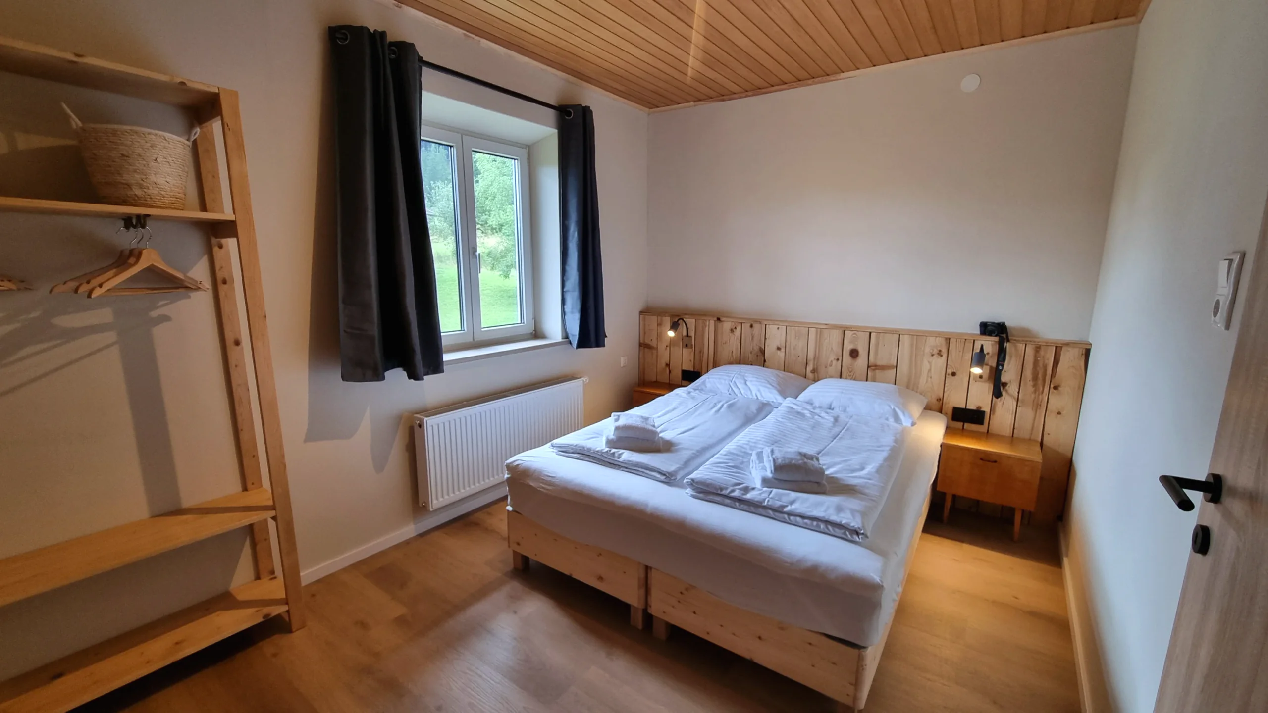 Schlafzimmer der Ferienwohnung 1 mit Holz-Kopfteil, offenem Regal und Fenster ins Grüne