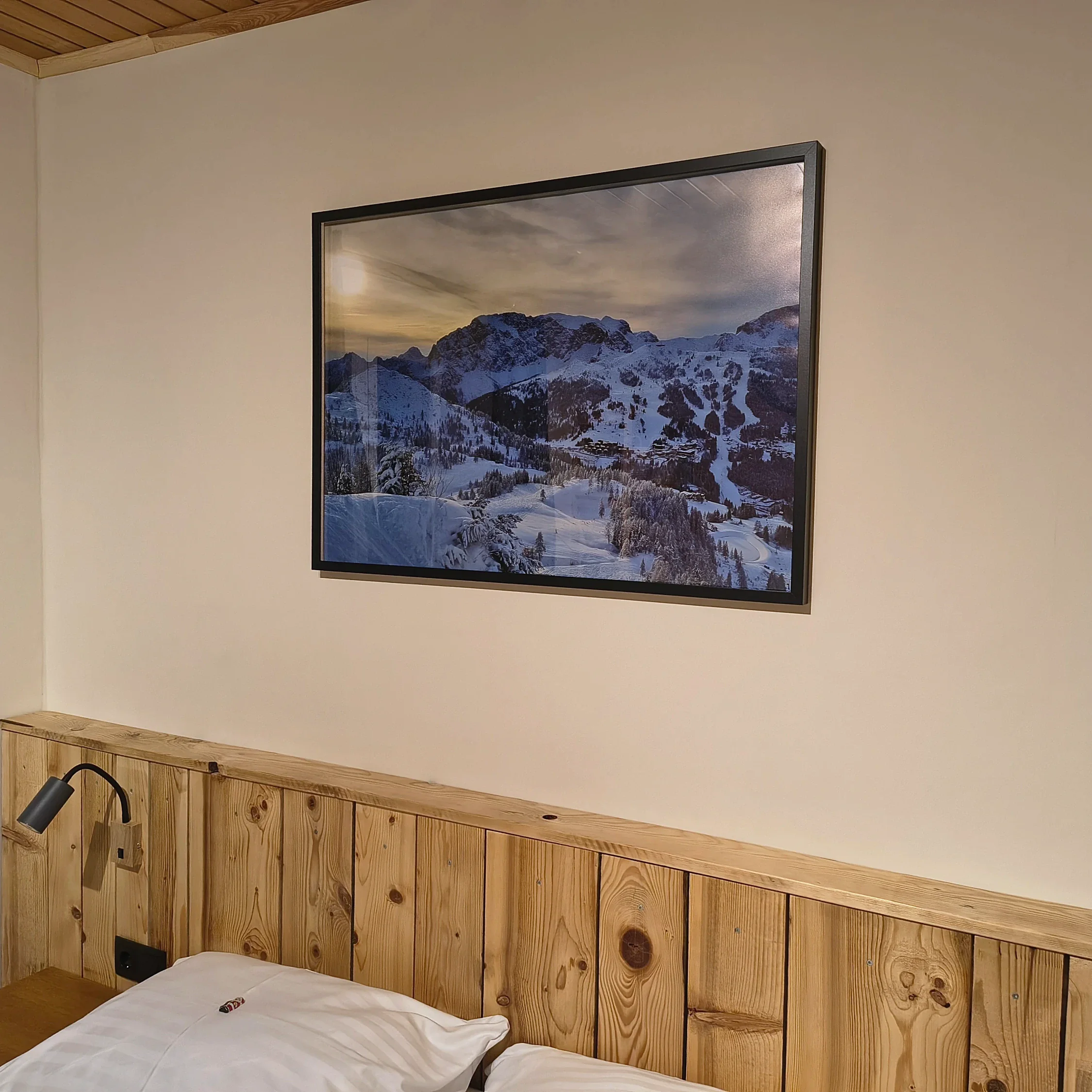 Doppelbett mit Kopfteil aus Holzlatten, darüber ein gerahmtes Foto verschneiter Berge