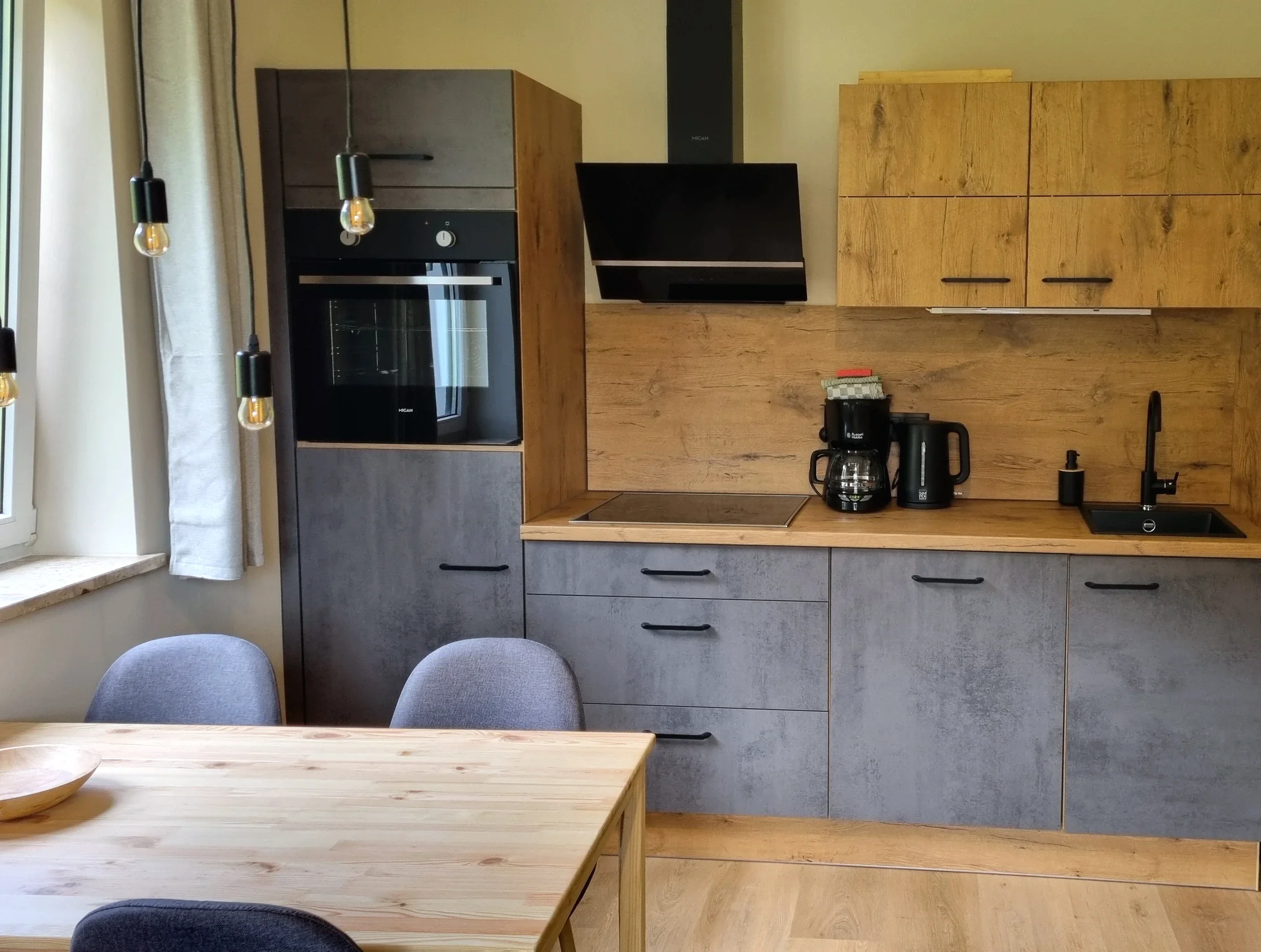 Küchenzeile der Ferienwohnung 2 mit Backofen, Dunstabzug, Kaffeemaschine und Esstisch davor