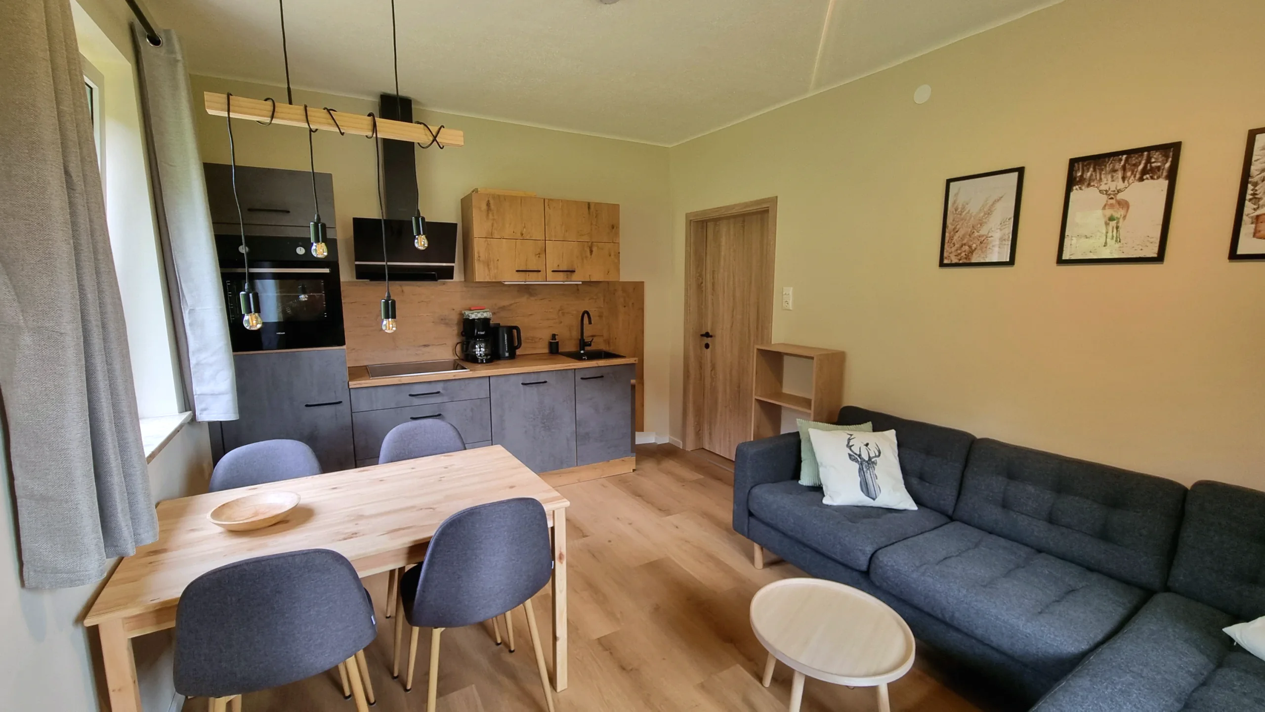 Offene Wohnküche der Ferienwohnung 2 mit Esstisch, Sofa und olivgrüner Wand