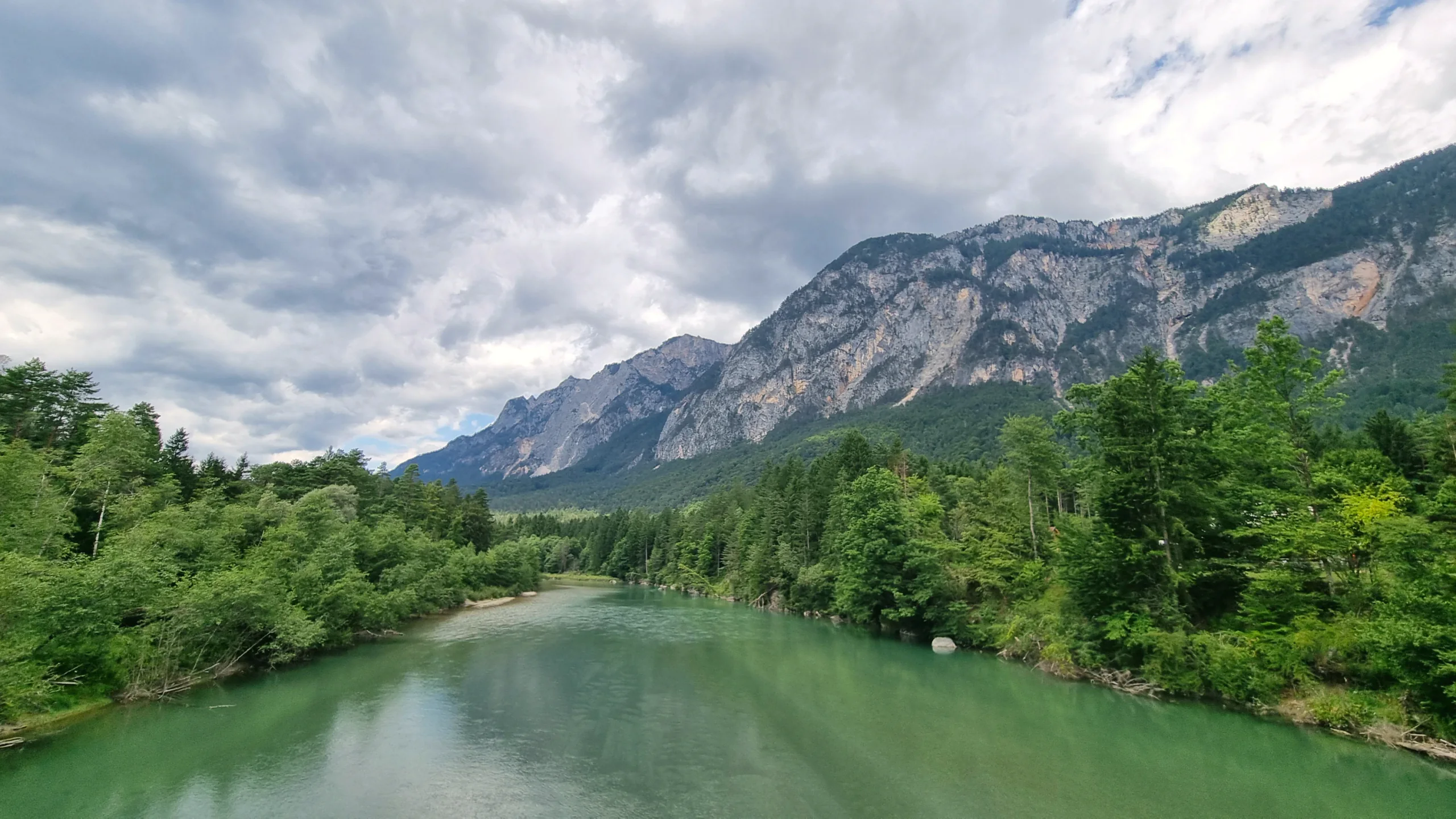 Die Gail mit grüntürkisem Wasser zwischen bewaldeten Ufern, dahinter eine helle Felswand