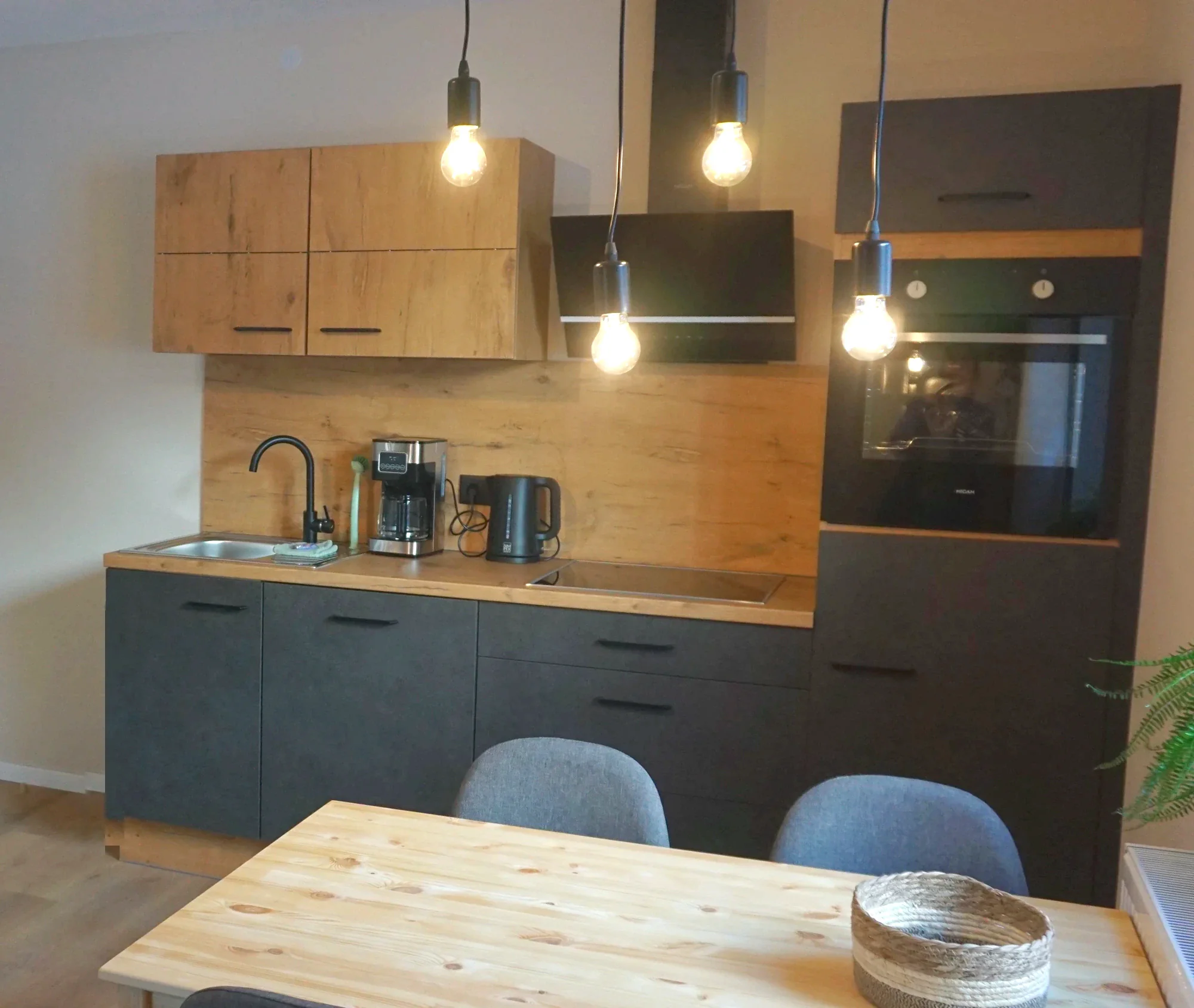 Küche der Ferienwohnung 1 mit Holzfronten, dunklen Unterschränken und Pendelleuchten über dem Esstisch