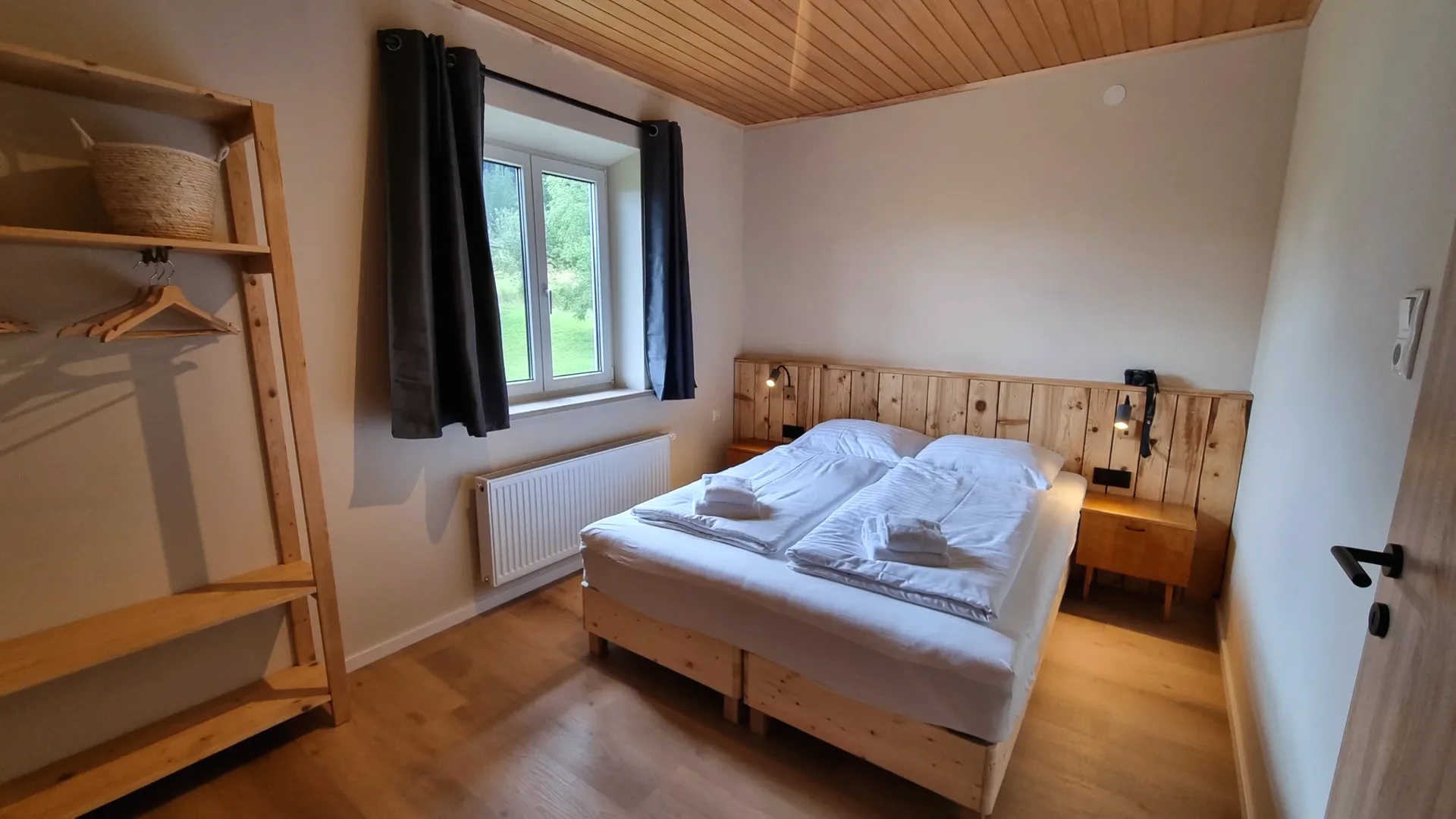 Schlafzimmer der Ferienwohnung 1 mit hölzernem Doppelbett, Leselampen und heller Holzdecke