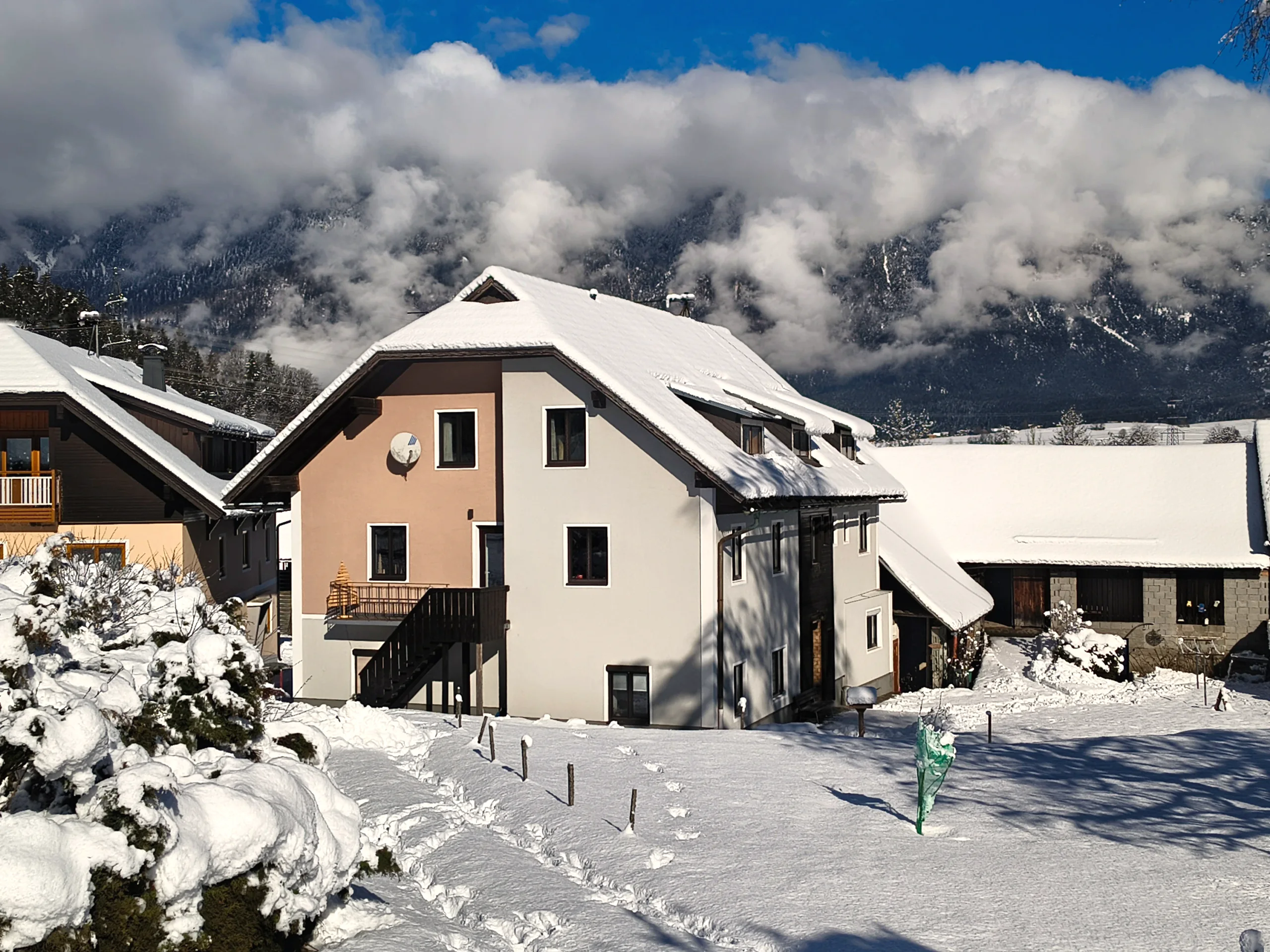 Haus Nampolach tief verschneit unter blauem Himmel, über der Bergkette dahinter hängt ein Wolkenband