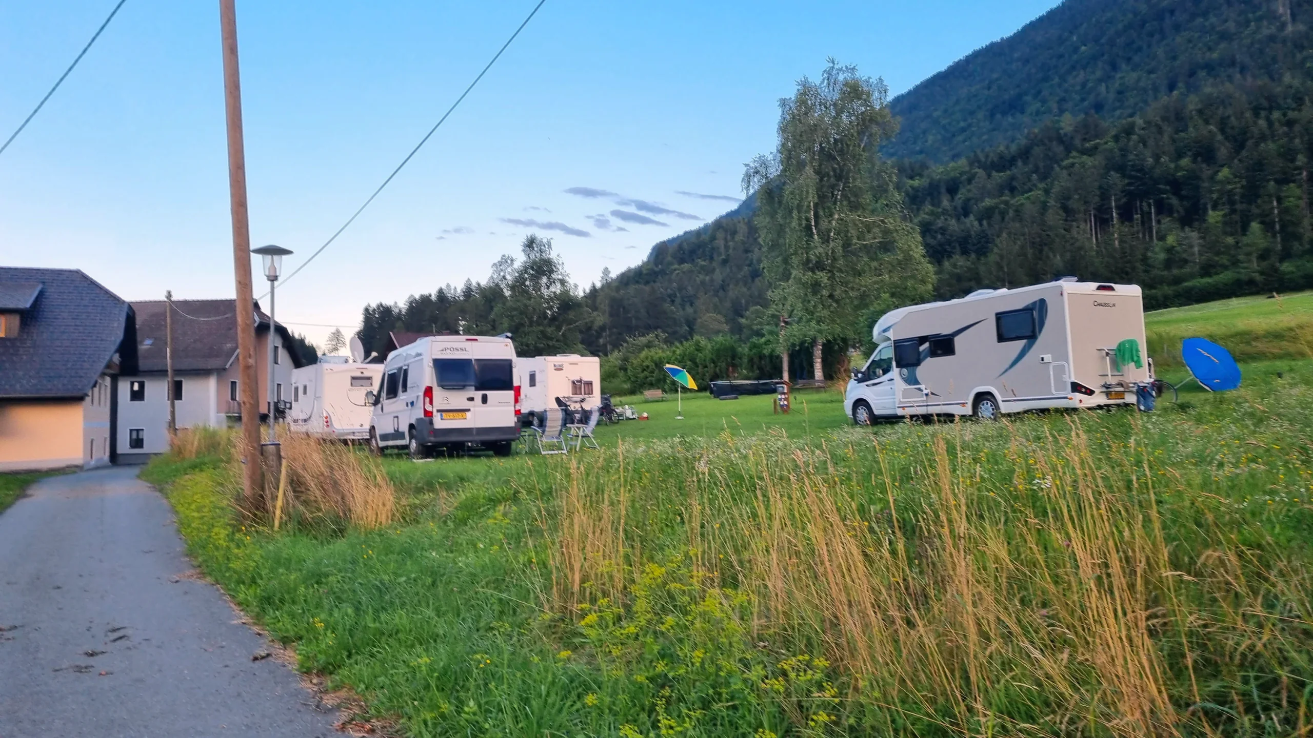 Wohnmobile auf der Stellplatzwiese in Nampolach im Abendlicht, dahinter ein bewaldeter Berghang