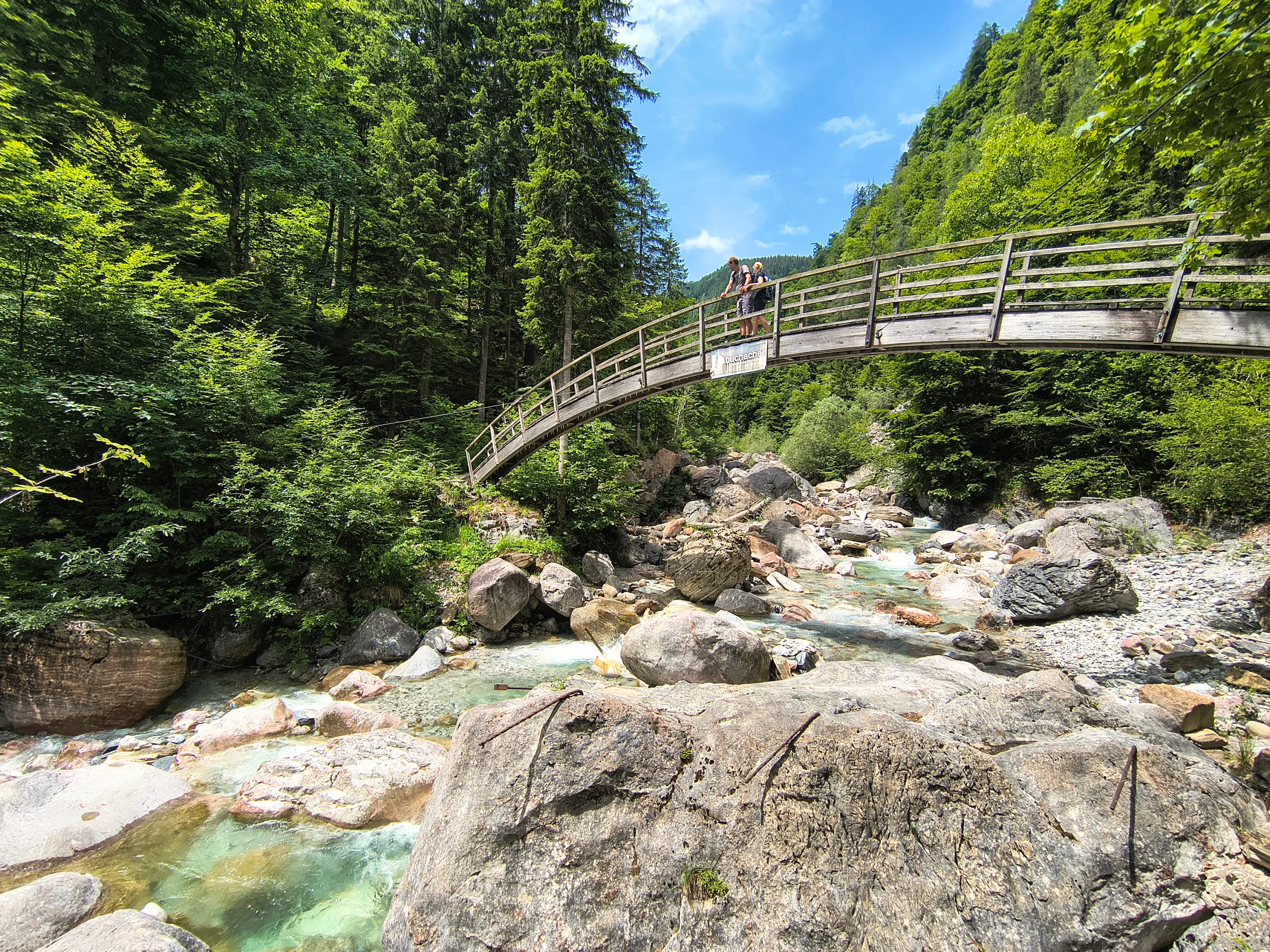 Holzbrücke über den türkisen Bach der Garnitzenklamm, ringsum Felsblöcke und steile Waldhänge