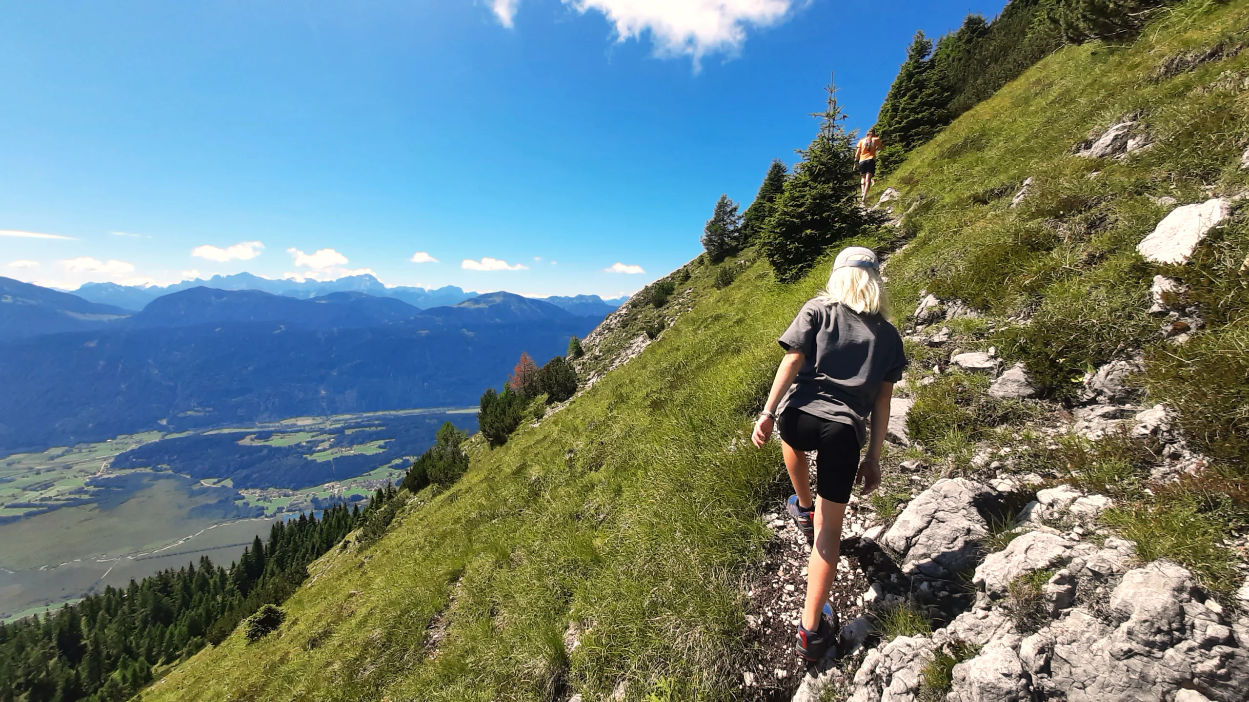 Wanderin auf einem schmalen Steig quer über den steilen Hang, tief unten liegt das Gailtal