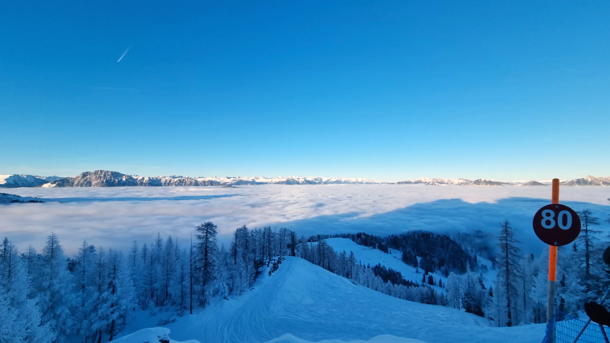 Präparierte Piste am Nassfeld, die über einem Wolkenmeer in die Tiefe zieht
