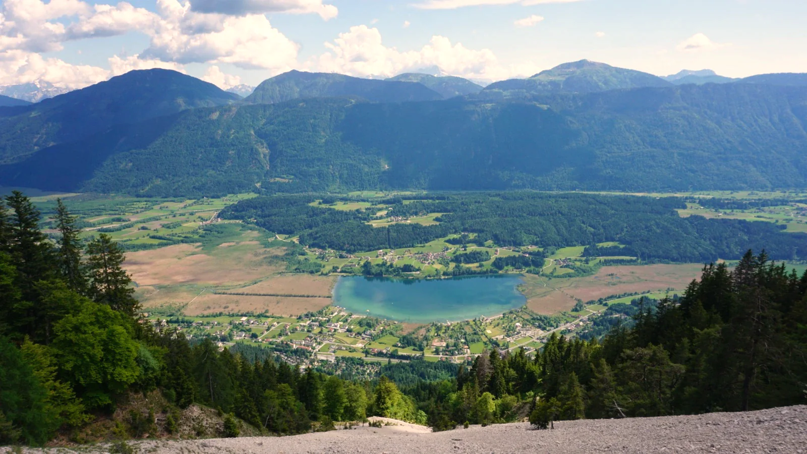 Blick von oben auf den Pressegger See im Talkessel, ringsum Wiesen, Wald und Häuser