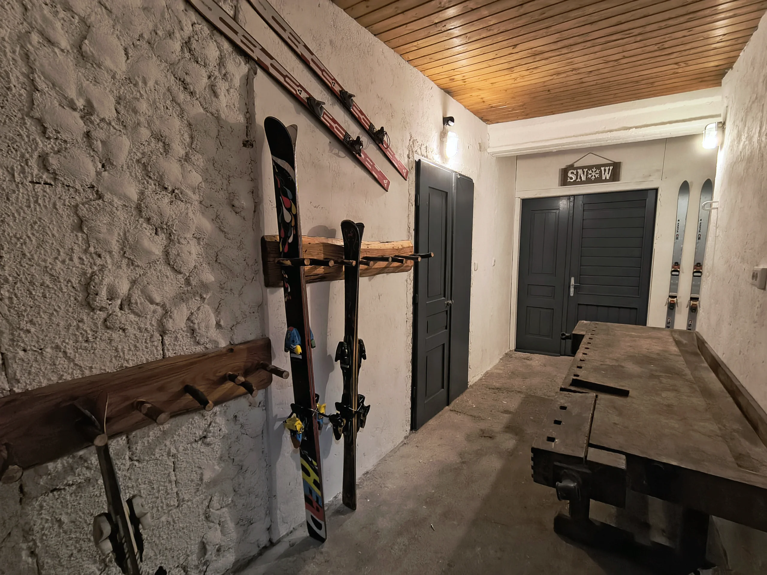 Skiraum im Haus: Ski und Snowboards an handgemachten Holzhaltern vor einer Bruchsteinwand, darüber eine Holzdecke