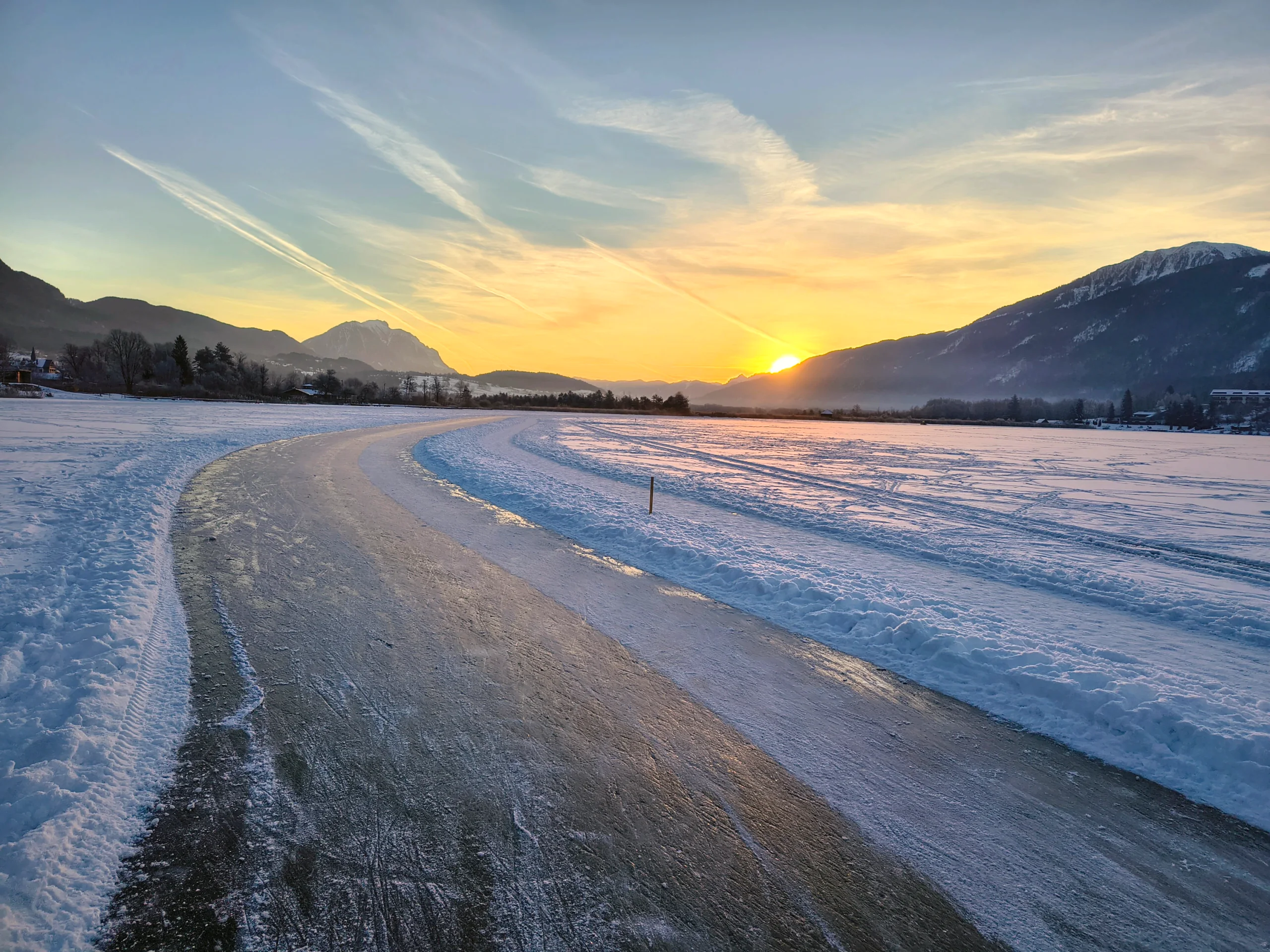 Sonnenaufgang über der verschneiten Ebene, der Weg im Vordergrund liegt noch im Schatten